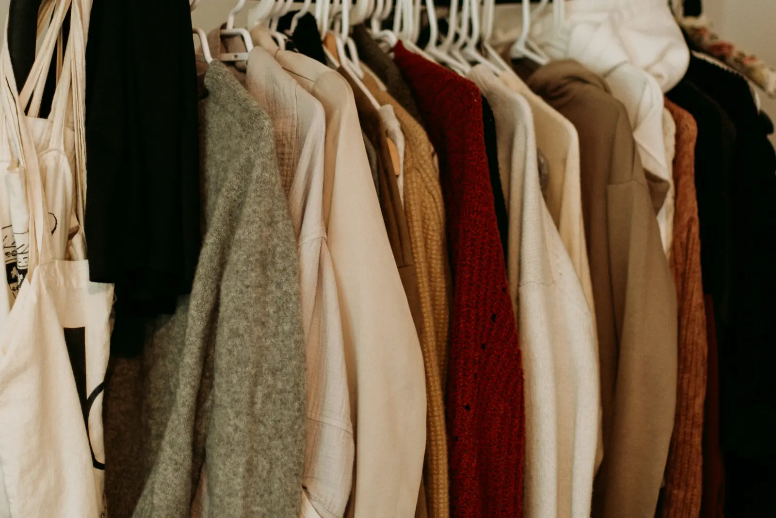 A rack of secondhand clothes in warm tones with a canvas tote bag.